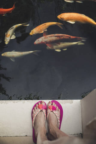 Nahaufnahme einer Frau in Flip Flops, die an einem Pool mit Kois steht, lizenzfreies Stockfoto