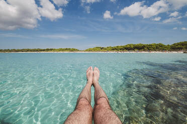 Beine eines Mannes vor dem Strand von Son Saura, Menorca, Spanien. - RAEF02327