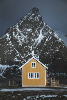 Norwegen, Moskenes, Lofoten, Sakrisoy, Traditionelle Rorbu-Fischerhütte mit dem Gipfel des Olstinden im Hintergrund - JRAF00017