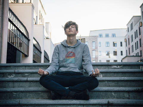 Teenager sitting on steps meditating in the city stock photo