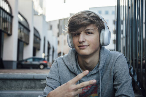 Portrait of teenager with headphones showing victory sign - ANHF00167