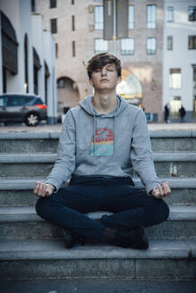 Teenager sitting on steps meditating in the city - ANHF00170