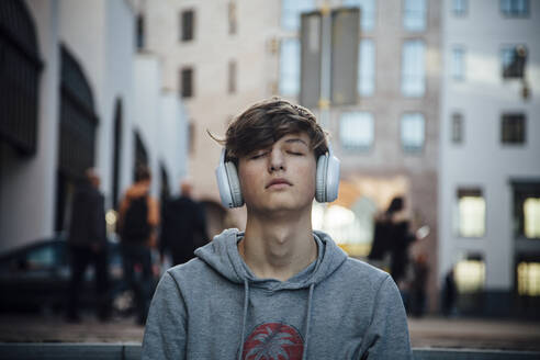 Portrait of teenager with headphones, sitting on steps in the city - ANHF00172