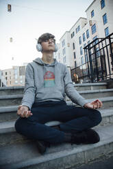 Teenager sitzt auf einer Treppe und meditiert in der Stadt und hört Musik - ANHF00174