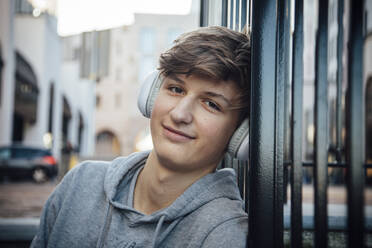 Porträt eines Teenagers mit Kopfhörern, der auf einer Treppe in der Stadt sitzt - ANHF00176
