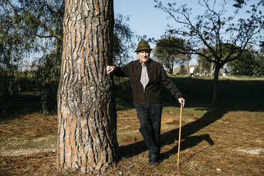 Alter Mann mit Gehstock, an einen Baum im Park gelehnt - JRFF04103