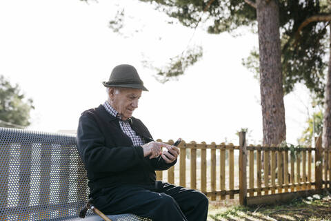 Alter Mann, der auf einer Bank sitzt und ein Smartphone benutzt, lizenzfreies Stockfoto