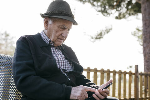 Alter Mann, der auf einer Bank sitzt und ein Smartphone benutzt, lizenzfreies Stockfoto