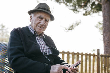 Alter Mann, der auf einer Bank sitzt und ein Smartphone benutzt - JRFF04115