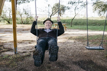 Old man swinging on playground in park - JRFF04116