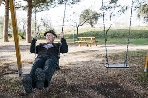 Alter Mann schaukelt auf einem Spielplatz im Park, lizenzfreies Stockfoto