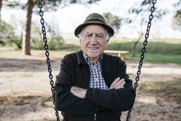 Old man sitting on swing in park, with arms crossed - JRFF04121