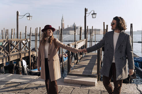 Junges Paar, das Hand in Hand an der Uferpromenade in Venedig, Italien, spazieren geht - MAUF03261