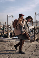 Junger Mann, der seine Freundin am Hafen von Venedig, Italien, huckepack nimmt - MAUF03265