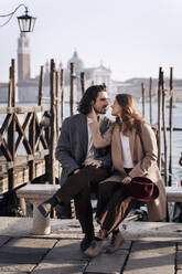 Junges Paar sitzt am Ufer in Venedig, Italien - MAUF03266