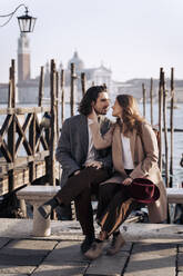 Young couple sitting at the waterfront in Venice, Italy - MAUF03266