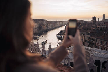 Junge Frau, die ein Handyfoto auf einem Balkon über der Stadt Venedig, Italien, macht - MAUF03311