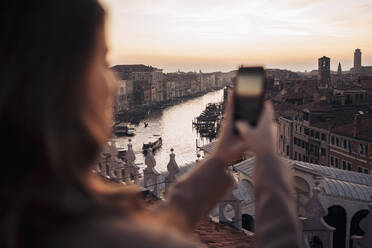 Young woman taking cell phone picture on a balcony above the city of Venice, Italy - MAUF03311