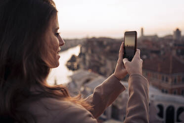 Junge Frau, die ein Handyfoto auf einem Balkon über der Stadt Venedig, Italien, macht - MAUF03312