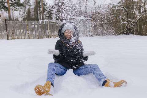 Glückliche Frau sitzt auf einem Schneefeld und spielt mit Schneebällen, lizenzfreies Stockfoto