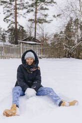 Glückliche Frau sitzt auf einem Schneefeld und spielt mit Schneebällen - KNTF04192