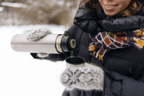 Crop-Ansicht von Frau gießt Tee in Thermobecher im Winter - KNTF04200