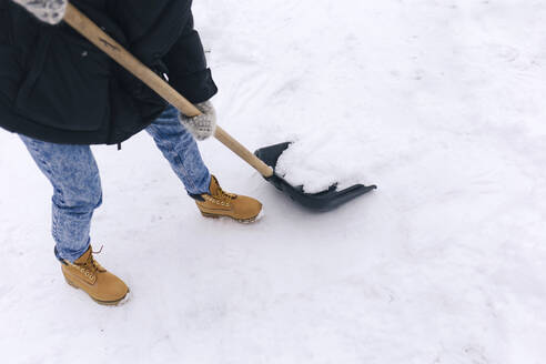 Crop-Ansicht einer Frau, die einen Gehweg mit einer Schneeschaufel räumt - KNTF04204