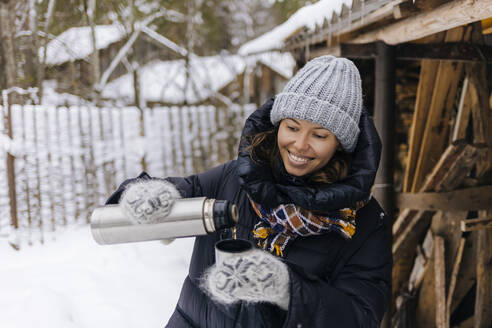 Porträt einer glücklichen Frau mit Thermoskanne im Winter - KNTF04215