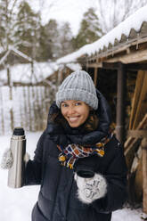 Porträt einer glücklichen Frau mit Thermoskanne im Winter - KNTF04216