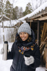 Portrait of happy woman with thermo flask in winter - KNTF04216