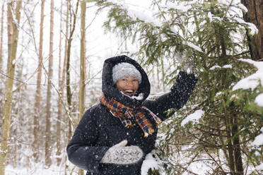 Porträt einer lachenden Frau im Winterwald, die den Schneefall genießt - KNTF04219
