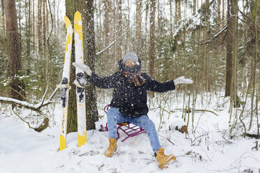Frau mit Skiern auf einem Schlitten sitzend im Winterwald, der Schnee in die Luft wirft - KNTF04229