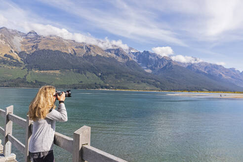 Neuseeland, Ozeanien, Südinsel, Otago, Lake Wakatipu, Neuseeländische Alpen, Glenorchy, Frau fotografiert Landschaft vom Steg aus - FOF11758