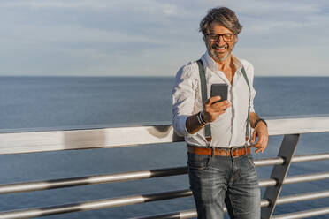 Lächelnder Mann mit Smartphone auf einem Bootssteg - DLTSF00435