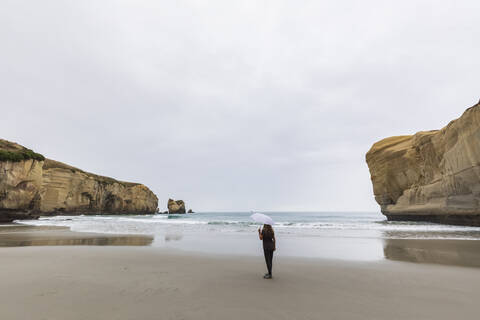Neuseeland, Ozeanien, Südinsel, Otago, Dunedin, Frau mit Sonnenschirm am Tunnel Beach, lizenzfreies Stockfoto