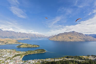 Neuseeland, Otago, Queenstown, Gleitschirmflieger fliegen über die Stadt am Seeufer mit Bergen im Hintergrund - FOF11803