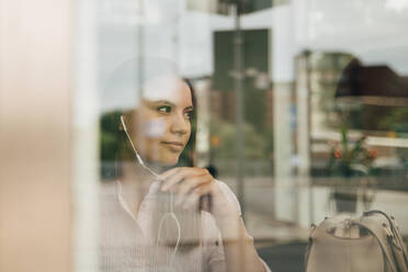 Nachdenkliche Geschäftsfrau mit Kopfhörern, gesehen durch ein Glasfenster im Büro - MASF16300