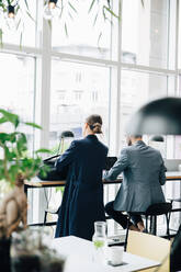 Rear view of businesswoman with bag by male colleague in cafeteria at office - MASF16305