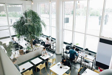 Blick von oben auf kreative Geschäftsleute, die an einem Schreibtisch in einem Coworking Space arbeiten - MASF16311