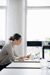 Side view of businesswoman listening music while working at desk in office - MASF16312