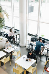 Blick von oben auf Geschäftsleute, die an einem Schreibtisch in einem Coworking Space arbeiten - MASF16315