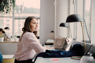 Nachdenkliche Geschäftsfrau sitzt am Schreibtisch in einem kreativen Büro - MASF16336