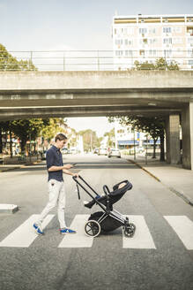 Volle Länge Seitenansicht des Mannes mit Smartphone beim Schieben Kinderwagen auf der Straße in der Stadt - MASF16348
