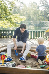 Vater und Sohn spielen auf einem Spielplatz im Park an einem sonnigen Tag - MASF16366