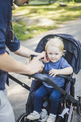 Mittelteil eines Mannes, der seinen auf einem Kinderwagen sitzenden Sohn in einem öffentlichen Park berührt - MASF16368