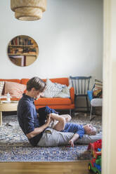 Seitenansicht eines Mannes, der einem Kleinkind beim Anziehen im heimischen Wohnzimmer hilft - MASF16373