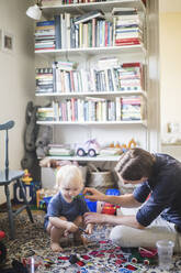 Mann putzt einem Kleinkind die Zähne, während es zu Hause im Wohnzimmer spielt - MASF16377