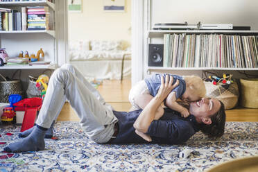 Lächelnder Mann auf dem Teppich liegend, während er mit seinem kleinen Sohn im Wohnzimmer zu Hause spielt - MASF16378
