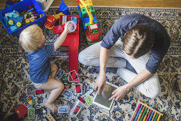 High angle view of blond baby boy playing toys by father using digital tablet in living room at home - MASF16380