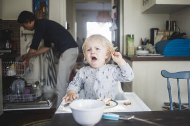 Weinendes männliches Kleinkind, das auf einem Hochstuhl in der Küche einer Wohnung sitzt und wegschaut - MASF16387